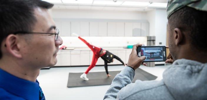 BSU biomechanics class with 1 student doing a cartwheel while another video records it and the professor looks on